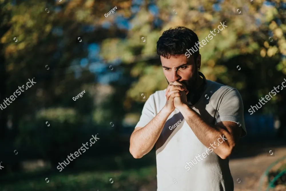 A man standing among trees with his hands pressed together in thought
