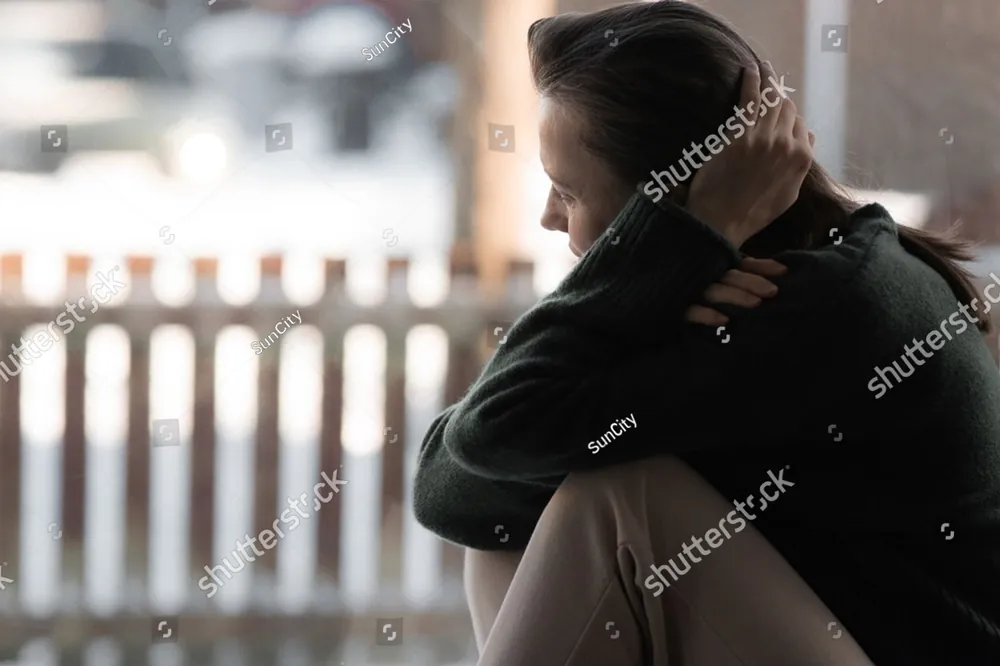 A woman sitting hunched on a bench with her arms around her knees