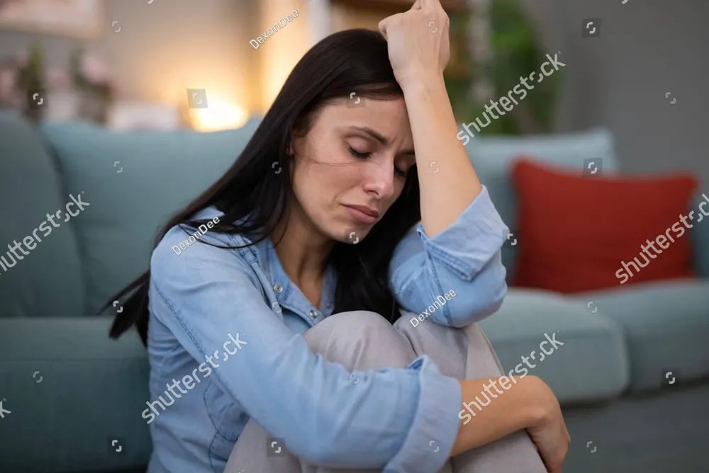 A woman sitting on the floor against the sofa, her head resting in her hand