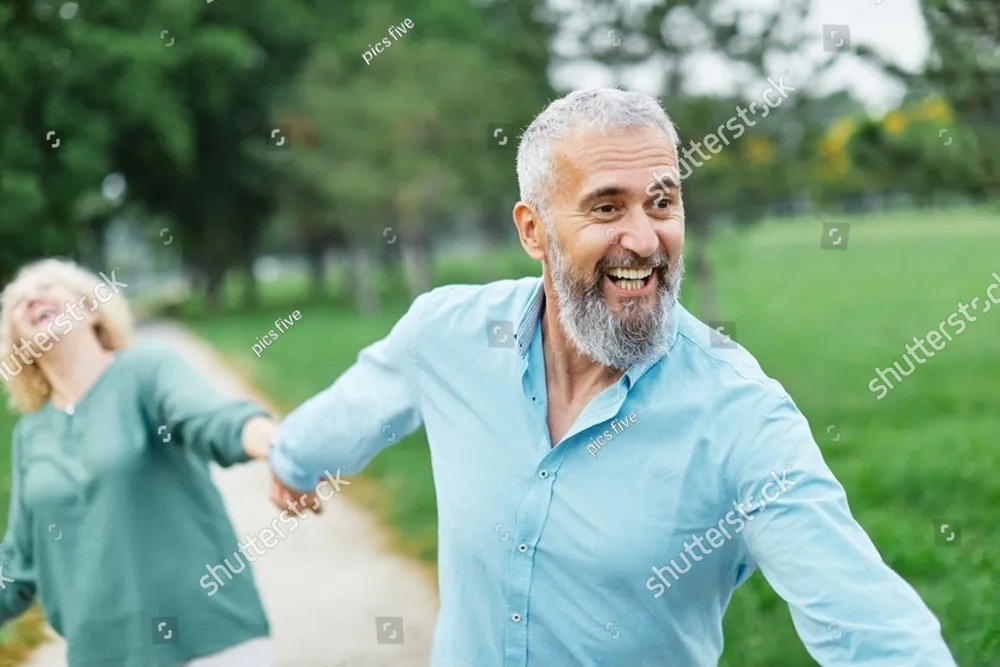 A smiling grey-haired man walking hand in hand with a woman in the park